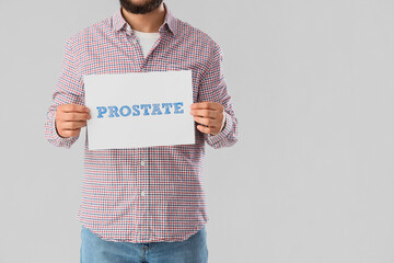 Young man holding paper with word PROSTATE on light background. Cancer awareness concept