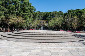 Wide view of a circular stepped stone platform surrounded by trees and benches at Parque El Dean in Guadalajara, Jalisco, Mexico