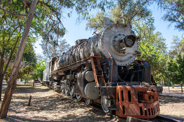 Rustic steam train locomotive sits under the shade of trees in Parque Independencia El Dean, a public park in Guadalajara