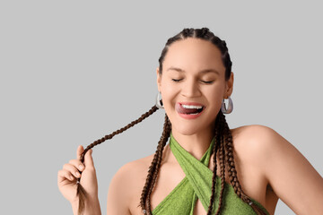 Stylish young woman with dreadlocks showing tongue on light background, closeup