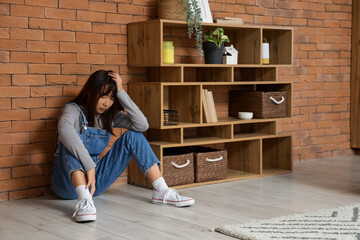 Young Asian woman with suicidal thoughts sitting near brick wall at home
