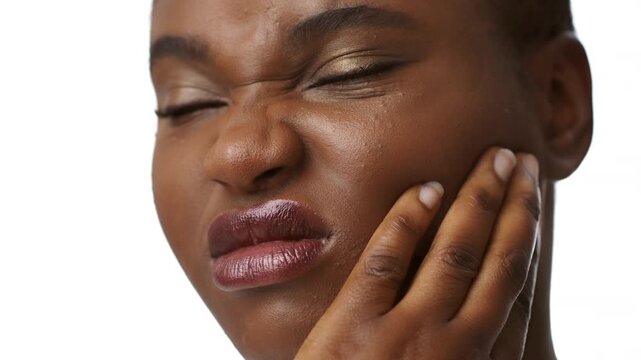 A millennial African American woman is showing a grimace of discomfort, holding her jaw in a healthcare context, have a toothache. Her expression conveys the experience of pain while being alone. - Powered by Adobe