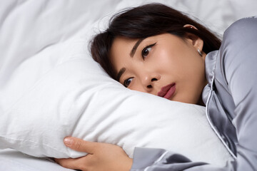 Young Asian woman with suicidal thoughts lying in bedroom, closeup