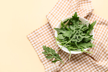 Bowl with fresh arugula leaves on beige background
