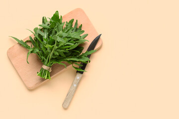 Wooden board with bunch of fresh arugula leaves on beige background