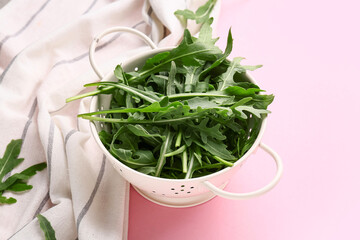 Colander with fresh arugula leaves on pink background, closeup