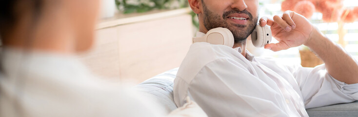 Young asian man with headphones sitting on sofa warmth while conversation with woman with cozy in living room at home, relationship and bonding, modern lifestyle.