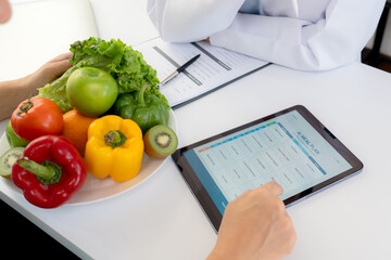 Asian nutritionist using tablet to explaining personalized meal plan with AI to patient during healthcare consultation, healthy lifestyle, woman dietitian showing nutrition plan with AI on tablet.