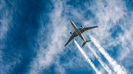 Naklejka premium Commercial airliner ascends through a cloudy blue sky, viewed from the wingtip with visible vapor trails.