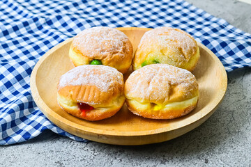 Close up view of three bomboloni doughnut with strawberry, pineapple and matcha filling on wooden...