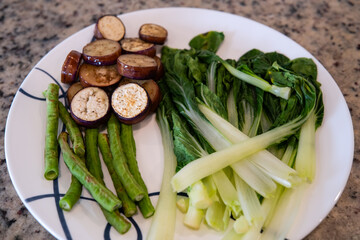 Freshly prepared vegetables ready for cooking on a white plate in a kitchen setting