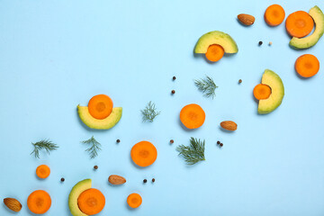 Slices of fresh carrot with avocado, dill, peppercorns and almond nuts on blue background