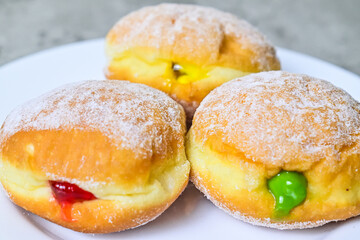 Extreme Close up view of three bomboloni doughnut with strawberry, pineapple and matcha filling on white plate. homemade. Italian stuffed donuts.