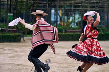 Portrait of a smiling young couple dressed as Chilean huasos,  joyfully dancing cueca outdoors....