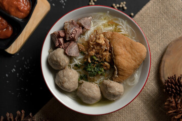 Top view, close-up of a bowl of Indonesian Bakso with fried tofu, beef, and meatballs on a rustic...