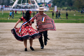 Portrait of a smiling young couple dressed as Chilean huasos,  joyfully dancing cueca outdoors....