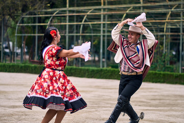 Portrait of a smiling young couple dressed as Chilean huasos,  joyfully dancing cueca outdoors....