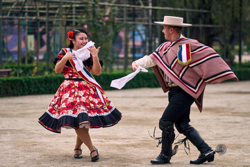Portrait of a smiling young couple dressed as Chilean huasos,  joyfully dancing cueca outdoors....