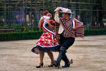 Portrait of a smiling young couple dressed as Chilean huasos,  joyfully dancing cueca outdoors....