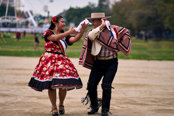 Portrait of a smiling young couple dressed as Chilean huasos,  joyfully dancing cueca outdoors....