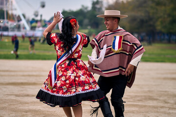Portrait of a smiling young couple dressed as Chilean huasos,  joyfully dancing cueca outdoors....