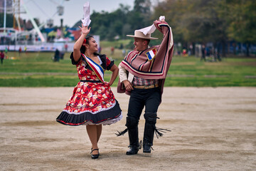 Portrait of a smiling young couple dressed as Chilean huasos,  joyfully dancing cueca outdoors....