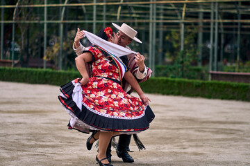 Portrait of a smiling young couple dressed as Chilean huasos,  joyfully dancing cueca outdoors....