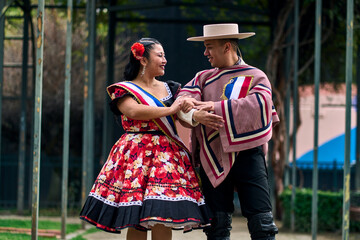 Portrait of a smiling young couple, dressed as Chilean huasos, looking at each other and posing...