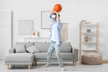Sporty young man in VR glasses playing with ball at home