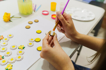 Artist carefully painting wooden daisy decorations with white acrylic paint, adding a touch of elegance to her craft project