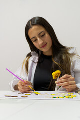 Concentrated craftswoman painting wooden discs and holding a yellow flower, creating art and crafts