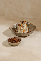 Vanilla ice cream with melted chocolate and caramel jam sprinkled with biscuit crumbs and biscuit pieces served next to it in a bowl with an aesthetic stone motif in photography art