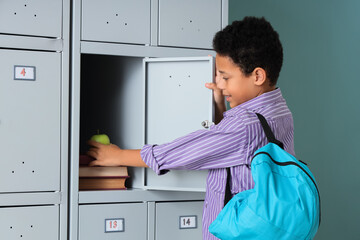 Teenage African-American schoolboy taking apple from locker on mint background
