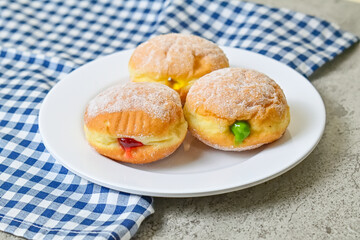 Close up view of three bomboloni doughnut with strawberry, pineapple and matcha filling on white plate. homemade. Italian stuffed donuts. grey or gray cement on the background. Napkin.