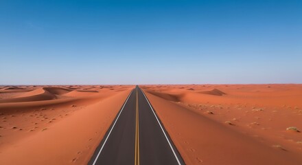 A long, straight asphalt road stretches through a vast desert landscape under a clear blue sky, leading towards the horizon.