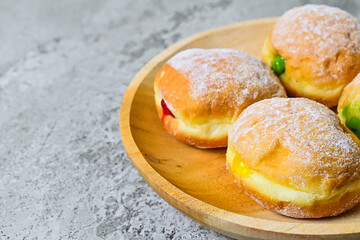Extreme Close up view of four bomboloni doughnut with strawberry, pineapple and matcha filling on wooden plate. homemade. grey or gray cement on the background. Copy space. Half.