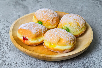 Close up view of four bomboloni doughnut with strawberry, pineapple and matcha filling on wooden plate. homemade. Italian stuffed donuts. grey or gray cement on the background.