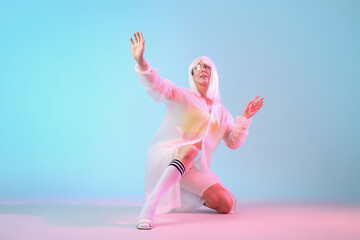 Fototapeta premium Young woman in futuristic costume with VR glasses sitting on blue background