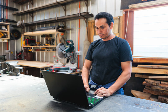 Latin carpenter working on a laptop in his woodworking shop