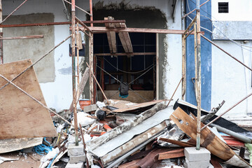 A messy atmosphere in front of a room that is being renovated, you can see several remaining building materials piled up and scaffolding still installed in front of the entrance to the room