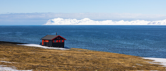 Beautiful landscape with of a hut along the coast with snowy mountains near Longyearbyen in the...