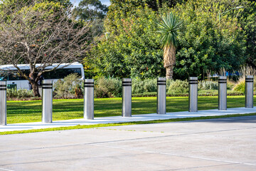 Stainless steel bollards lined up in a landscaped public space, separating pedestrian areas from vehicle access. Fixed equipment enhances safety while blending with modern park or campus environments.