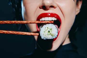 A stylish woman with red lips holding sushi with chopsticks, showcasing a vibrant eating experience with a modern touch.