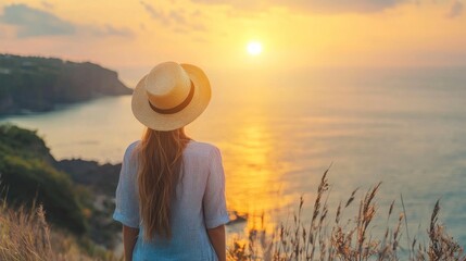 A woman in a white dress standing on a cliff overlooking the ocean at sunset.