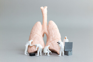 Tiny hazmat-suited figures examine a human lung model, representing respiratory health, lung disease research, and medical innovation