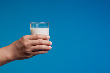 Hand holding clear glass of soy milk against blue background, concept for vegan drink and health.