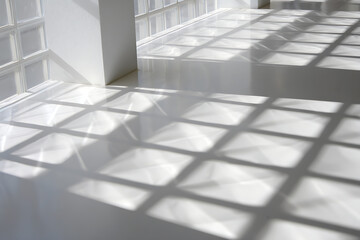 Obraz premium Sunlight casting geometric grid patterns of light and shadow across a clean white floor and wall in an empty room