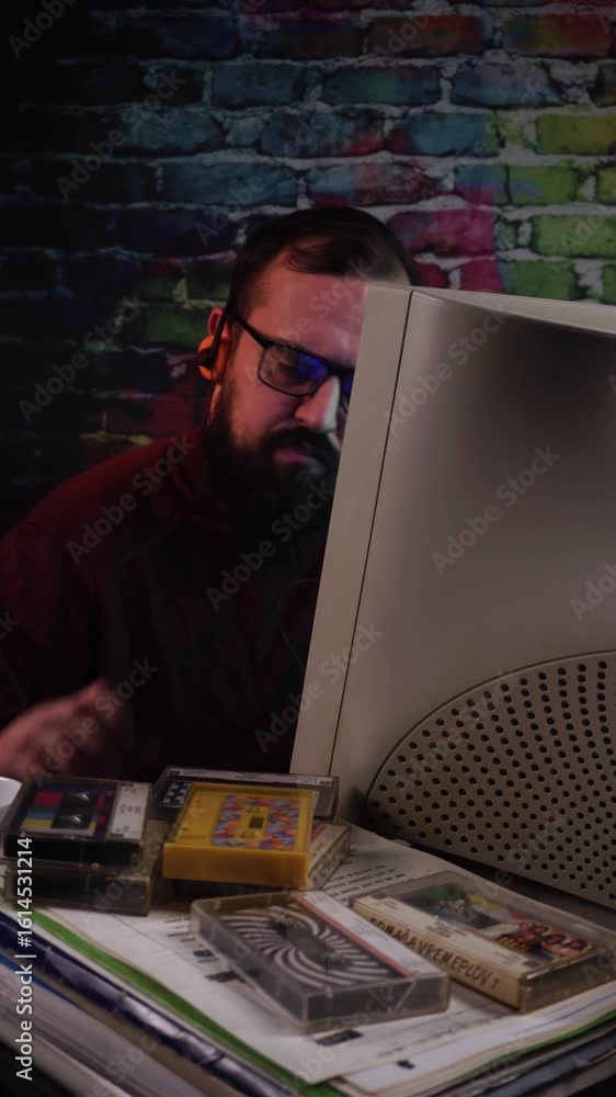 Poster man from 1980's listening music from audio cassette tapes in front of desktop computer, vertical vie