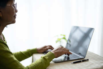 Mature Asian Woman Wearing Glasses Using Laptop at Home for Digital Engagement.