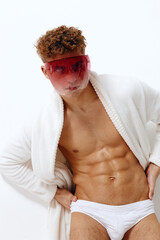 Confident young male model posing in a white bathrobe and red tinted sunglasses. Fashion and...
